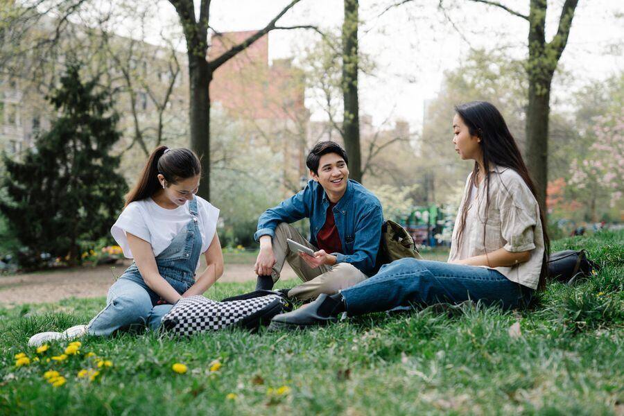 Tres personas conversando cara a cara, sentadas en el pasto.